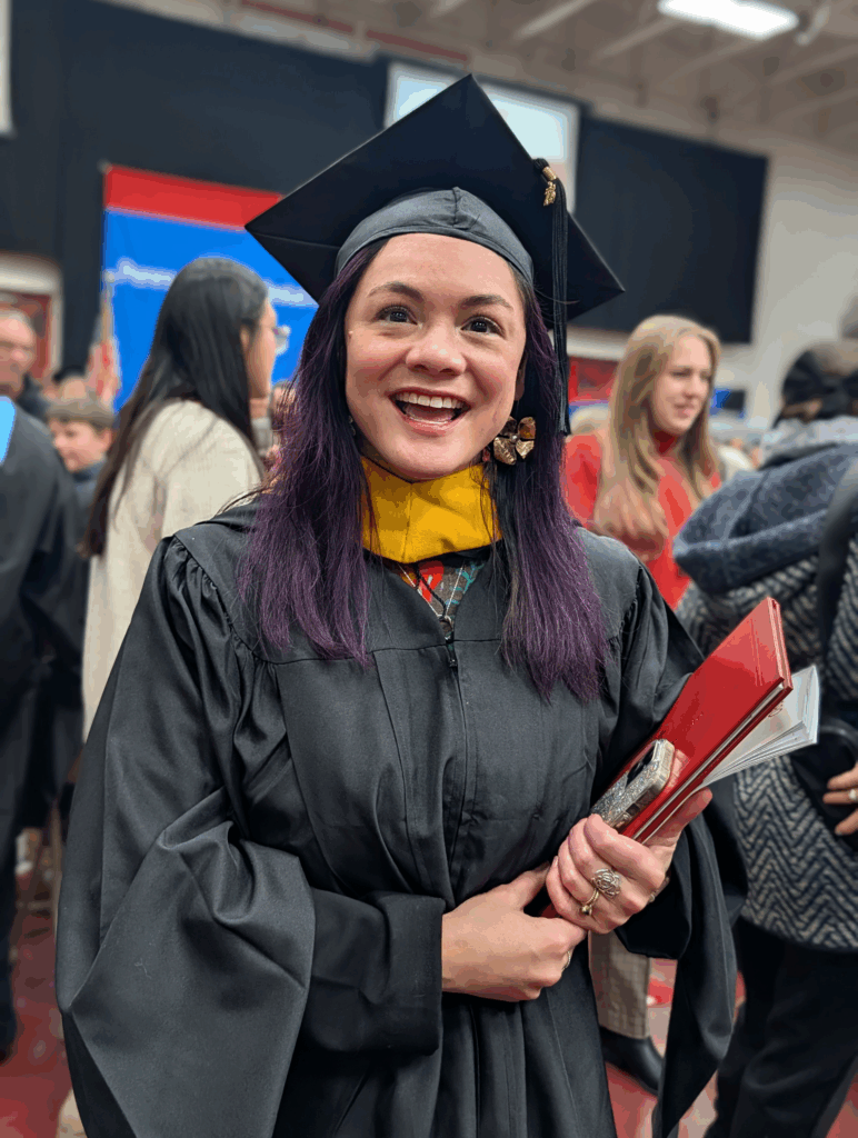 Melissa smiling holding her diploma while wearing her cap and gown